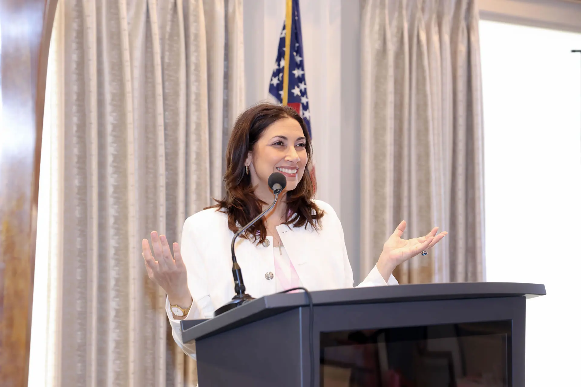 Leslie Alvarez, a professional motivational speaker, is shown smiling and gesturing openly from a lectern while delivering an inspiring message.